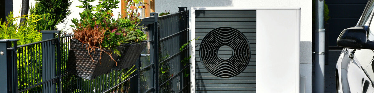Wärmepumpe vor einem Neubau mit Garten, bereit zur effizienten Wärmeversorgung des Hauses.