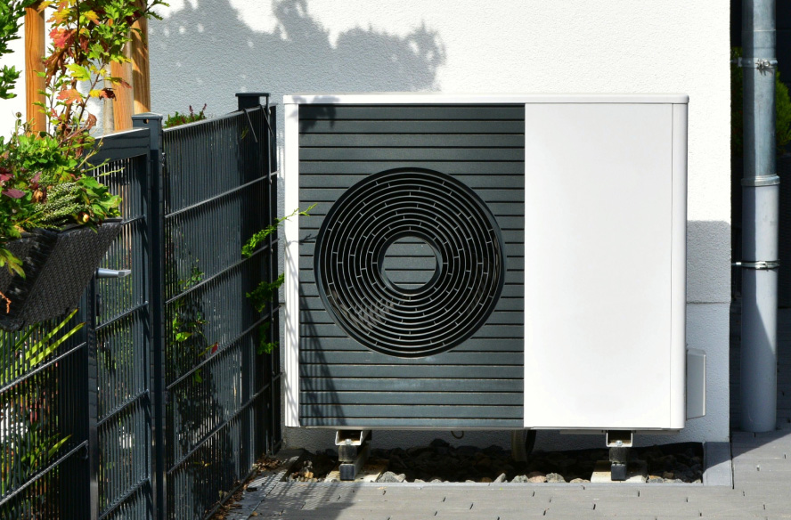 Wärmepumpe vor einem Haus mit Garten, bereit zur effizienten Wärmeversorgung des Hauses.